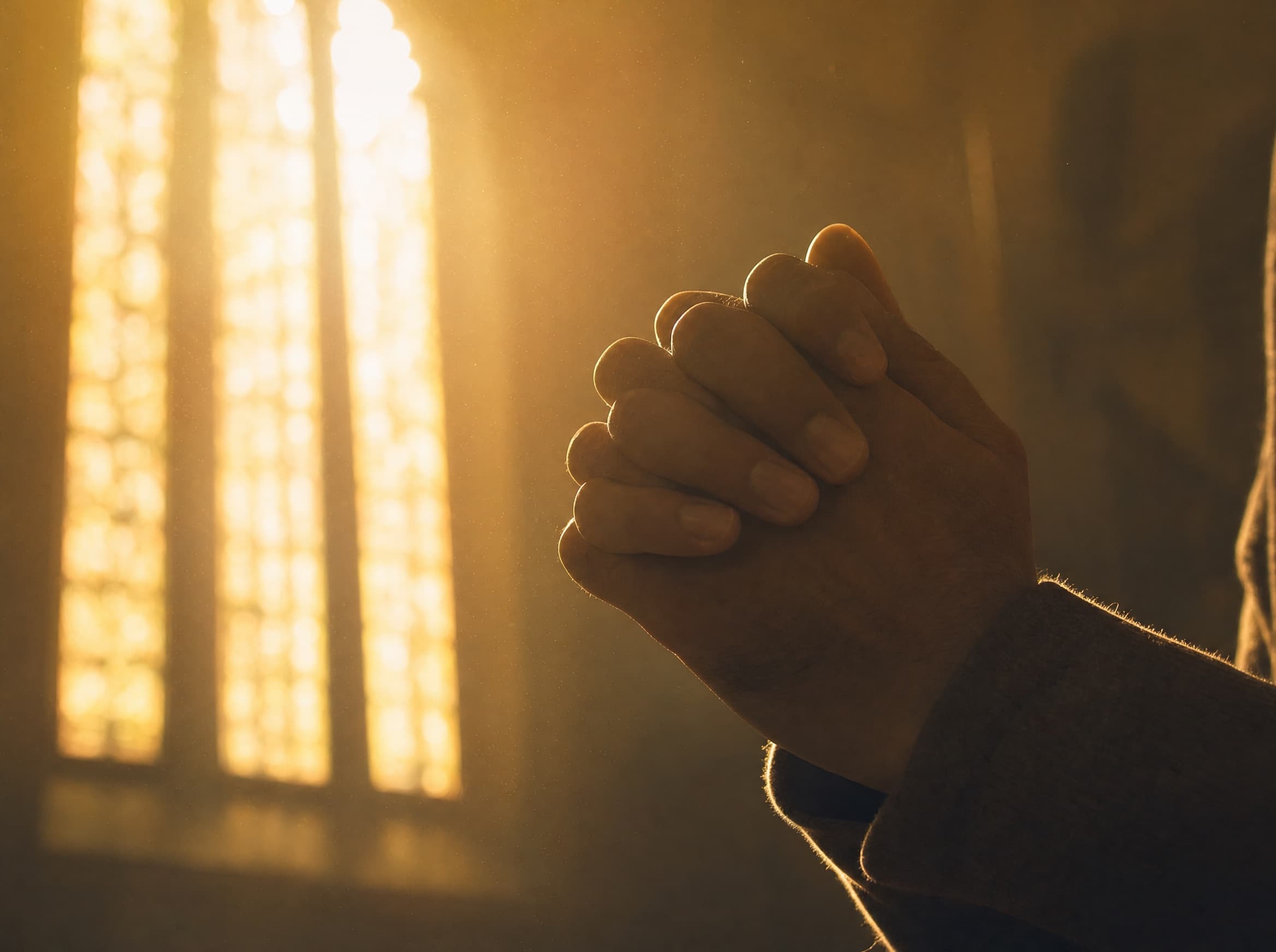 Betende Hände im goldenen Licht eines Kirchenfensters
